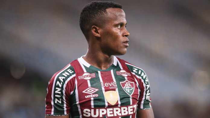 Jhon Arias com a camisa do Fluminense. No uniforme, há o patch da Libertadores de 2023, a logo-marca da Umbro e também o patrocino das marcas Leve, Superbet, Frescatto e Zinzane. O uniforme do Fluminense é listrado em verde, branco e grená. O escudo fica localizado no lado esquerdo do peito, com a sigla FFC em fonte gótica.